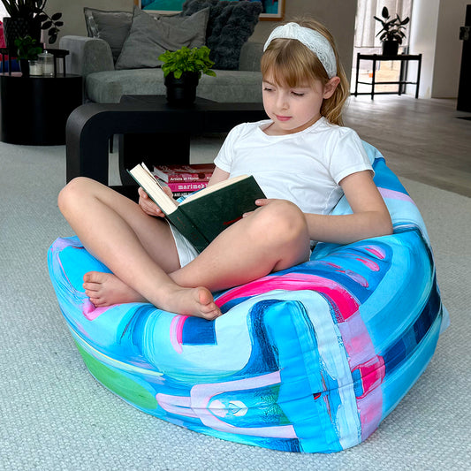 Child reading a book on a colorful bean bag chair in a living room.